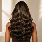 Black woman wearing a full brown highlight loose body wave wig with a defined left C part.