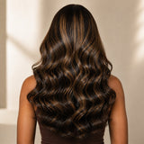 Black woman wearing a full brown highlight loose body wave wig with a defined left C part.