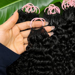 Close-up of a Black woman holding a single bundle of Burmese curly crochet hair, showing natural curls and shine, pink loop attachment visible, green leaf background.