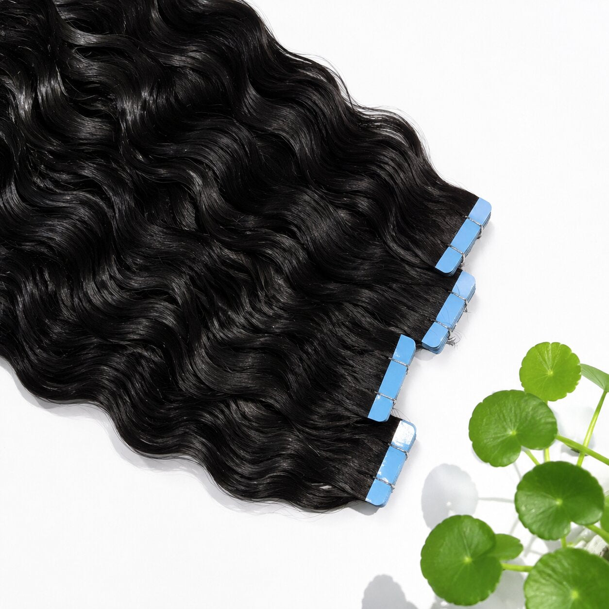 Flat lay of black wavy tape-in hair extensions on a white background. Hair strands are glossy and uniform, with neatly stacked blue adhesive tabs, showcasing premium human hair texture.