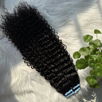 Flat lay of curly black tape-in hair extensions on a soft white background with natural sunlight. Features icons highlighting natural volume, seamless blend, quick application, and long-lasting beauty. Zoomed circle shows full, healthy hair ends. Modern, minimalistic layout emphasizing premium quality and natural shine.