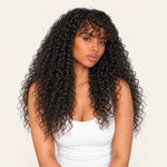 Model wearing a natural black kinky curly wig with curly bangs and a white tank top.
