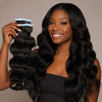 Portrait of a confident Black woman with long, voluminous wavy hair extensions, shiny and naturally blended, wearing a black strapless top against a minimal indoor background with soft natural lighting, showcasing healthy hair texture.