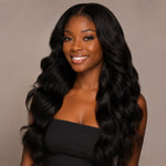 Portrait of a confident Black woman with long, voluminous wavy hair extensions, shiny and naturally blended, wearing a black strapless top against a minimal indoor background with soft natural lighting, showcasing healthy hair texture.