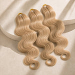 Three #27/#613 blonde blend body wave crochet human hair bundles arranged on a warm beige studio pedestal