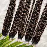 Top-down display of multiple Feathered Crochet Hair bundles with deep brown and caramel highlights, coiled feathered curls, shiny and smooth texture on white faux-fur background with tropical leaves